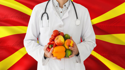 Doctor is holding fruits and vegetables in hands with Macedonia flag background. National healthcare concept, medical theme.