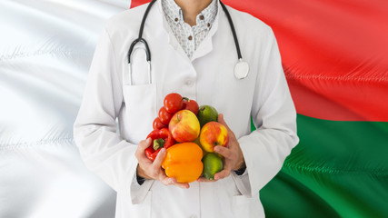 Doctor is holding fruits and vegetables in hands with Madagascar flag background. National healthcare concept, medical theme.
