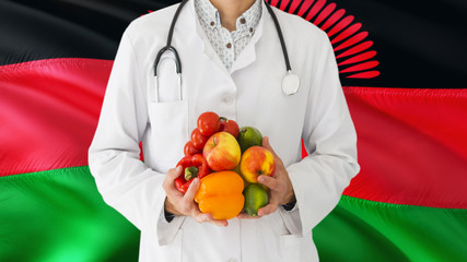 Doctor is holding fruits and vegetables in hands with Malawi flag background. National healthcare concept, medical theme.