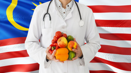 Doctor is holding fruits and vegetables in hands with Malaysia flag background. National healthcare concept, medical theme.