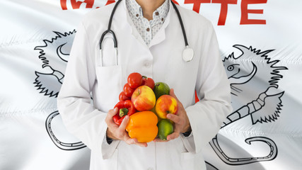 Doctor is holding fruits and vegetables in hands with Mayotte flag background. National healthcare concept, medical theme.