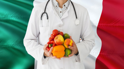 Doctor is holding fruits and vegetables in hands with Mexico flag background. National healthcare concept, medical theme.