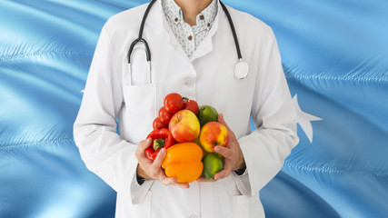 Doctor is holding fruits and vegetables in hands with Micronesia flag background. National healthcare concept, medical theme.