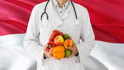 Doctor is holding fruits and vegetables in hands with Monaco flag background. National healthcare concept, medical theme.