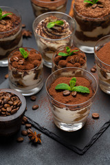 Group of portions of Classic tiramisu dessert in a glass cup on stone board on concrete background
