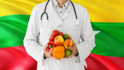 Doctor is holding fruits and vegetables in hands with Myanmar flag background. National healthcare concept, medical theme.