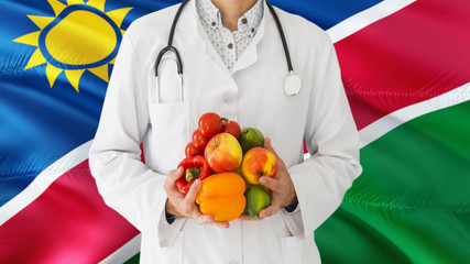 Doctor is holding fruits and vegetables in hands with Namibia flag background. National healthcare concept, medical theme.