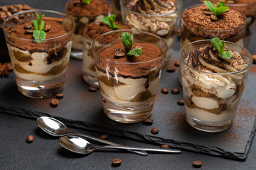 Group of portions of Classic tiramisu dessert in a glass cup on stone board on concrete background
