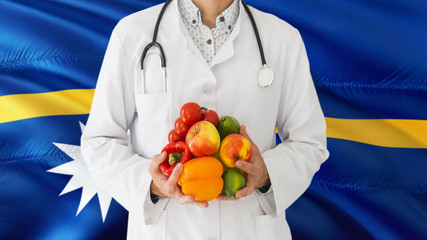 Doctor is holding fruits and vegetables in hands with Nauru flag background. National healthcare concept, medical theme.