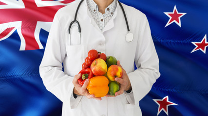 Doctor is holding fruits and vegetables in hands with New Zealand flag background. National healthcare concept, medical theme.
