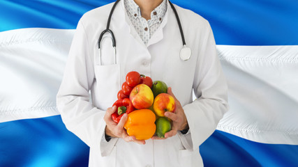 Doctor is holding fruits and vegetables in hands with Nicaragua flag background. National healthcare concept, medical theme.