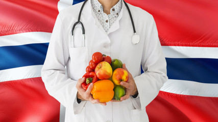Doctor is holding fruits and vegetables in hands with Norway flag background. National healthcare concept, medical theme.