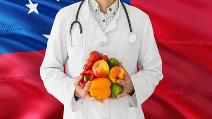 Doctor is holding fruits and vegetables in hands with Samoa flag background. National healthcare concept, medical theme.