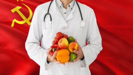 Doctor is holding fruits and vegetables in hands with Soviet Union flag background. National healthcare concept, medical theme.