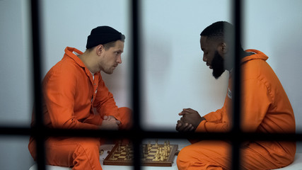 Caucasian and afro-american jail inmates playing chess in cell, prison hobby