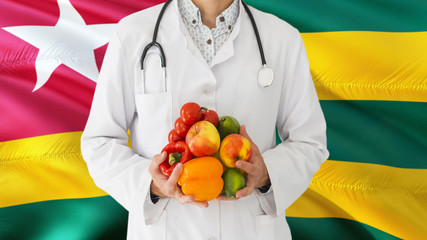 Doctor is holding fruits and vegetables in hands with Togo flag background. National healthcare concept, medical theme.