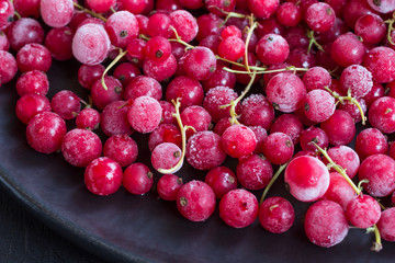 Frozen red currants in a black plate on a black background