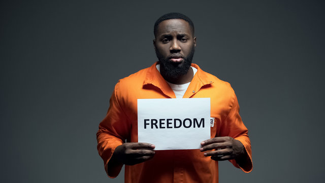 Black imprisoned male holding freedom sign in cell, asking for help human rights