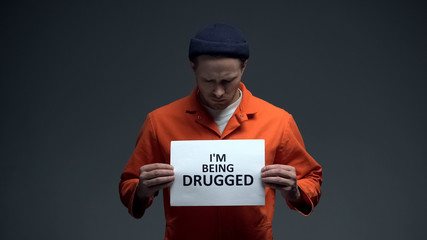 Fototapeta na wymiar European imprisoned man holding I am being drugged sign in cell, warning, addict