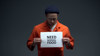 Fototapeta na wymiar Male prisoner holding Need normal food sign, ill treatment in jail, starving
