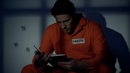 Imprisoned male reading book in jail cell, available hobby, self-education