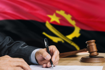 Judge writing on paper in courtroom with Angola flag background. Wooden gavel of equality theme and legal concept.