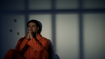 Caucasian male prisoner praying, feeling guilty about crimes, asking for mercy