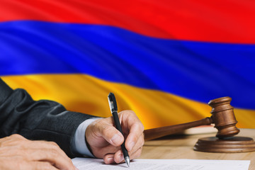 Judge writing on paper in courtroom with Armenia flag background. Wooden gavel of equality theme and legal concept.