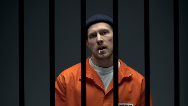 Arrogant imprisoned male with toothpick showing bad manners, splitting on floor
