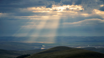 in the mountains, the sun's rays make their way through the clouds