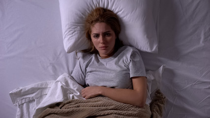 Lady feeling unwell lying in bed covered with blankets, menstrual pain, topview