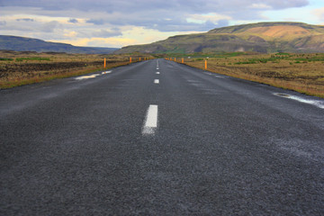 Icelandic landscape. Direct asphalt road of the Golden Ring rout. Mountains around. Evening. Painted sky with flowers. Summer.