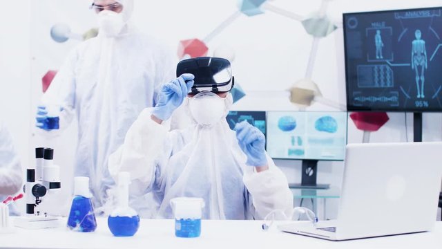Female scientist with virtual reality headset in modern chemistry laboratory. Scientist holding test tubes with blue solution in the background.