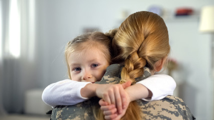 Little daughter hugging soldier mother in camouflage uniform, war homecoming