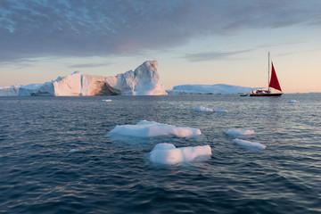 A small boat among icebergs. Sailboat cruising among floating icebergs in Disko Bay glacier during...