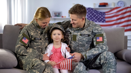 Smiling military parents looking at cute daughter with american flag, patriots