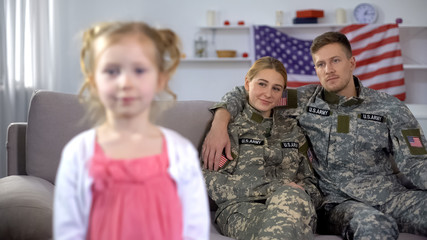 Joyful parents in US military uniform admiring little daughter looking at camera