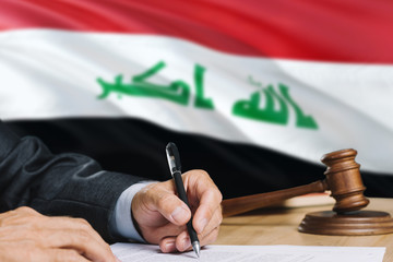 Judge writing on paper in courtroom with Iraq flag background. Wooden gavel of equality theme and...