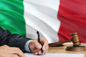Judge writing on paper in courtroom with Italy flag background. Wooden gavel of equality theme and...