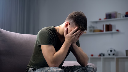 Depressed soldier crying at home, remembering dead fellows and horrors of war