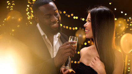 Smiling african-american male offering Asian lady glass of champagne, flirt