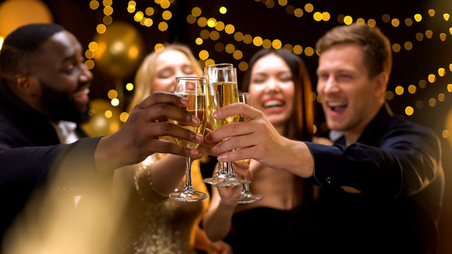 Happy multi-ethnic company clinking beverage glasses, celebrating New Year