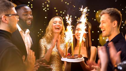 Pretty woman in party hat carrying cake with fire candles, celebrating birthday