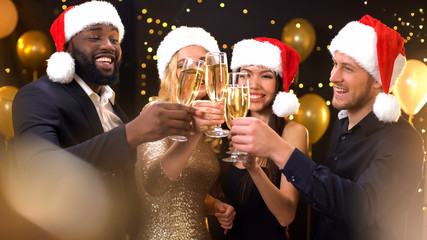 Multiracial friends in santa hats clinking champagne glasses, New Year party