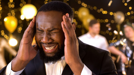Afro-american man feeling headache closeup, irritated by noisy party, hangover