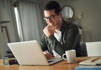 Happy handsome smiling man working on laptop at home