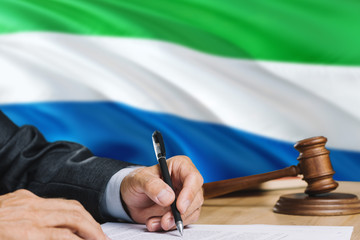 Judge writing on paper in courtroom with Sierra Leone flag background. Wooden gavel of equality theme and legal concept.