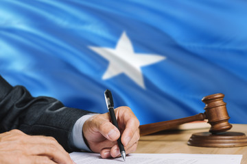 Judge writing on paper in courtroom with Somalia flag background. Wooden gavel of equality theme and legal concept.