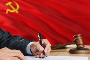 Judge writing on paper in courtroom with Soviet Union flag background. Wooden gavel of equality theme and legal concept.