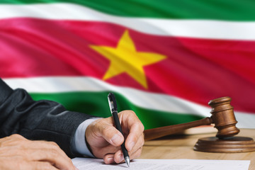 Judge writing on paper in courtroom with Suriname flag background. Wooden gavel of equality theme and legal concept.